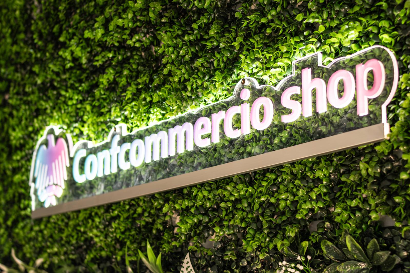 Insegna luminosa Confcommercio shop sulla parete verde del set